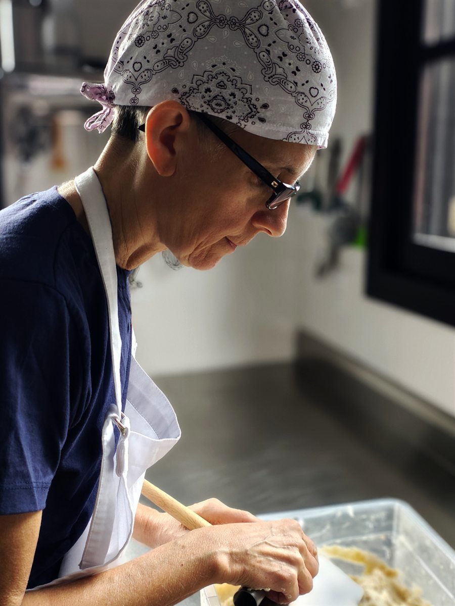 Marcela de perfil, concentrada, sovando a massa de fermentação natural na cozinha do Beco da Marcela