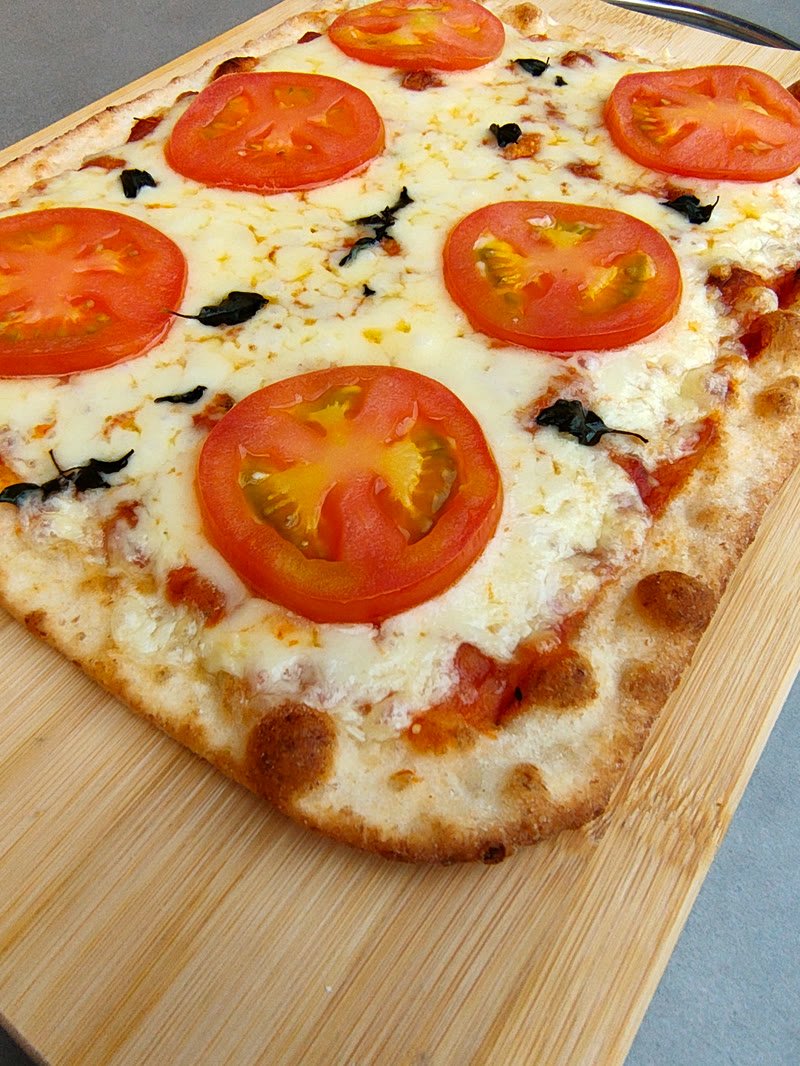 Pizza Romana Crocante Marguerita assada, com muçarela derretida, rodelas de tomate e manjericão, sobre tábua de bambu
